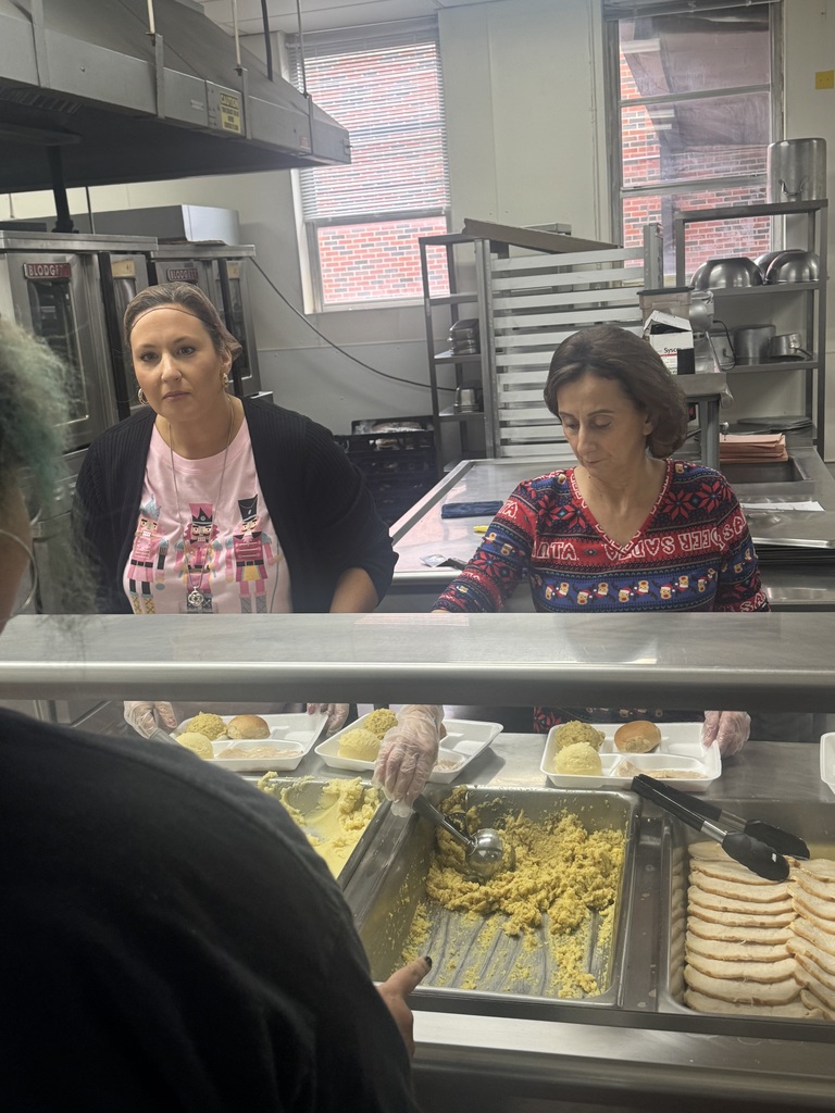 Two women prepare food at a kitchen counter. One holds a serving spoon and the other wears a pink shirt.