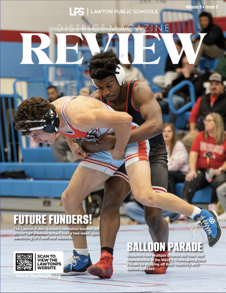 Magazine cover with two wrestlers grappling in a gym. One in red, one in black. Spectators watch from blue bleachers.