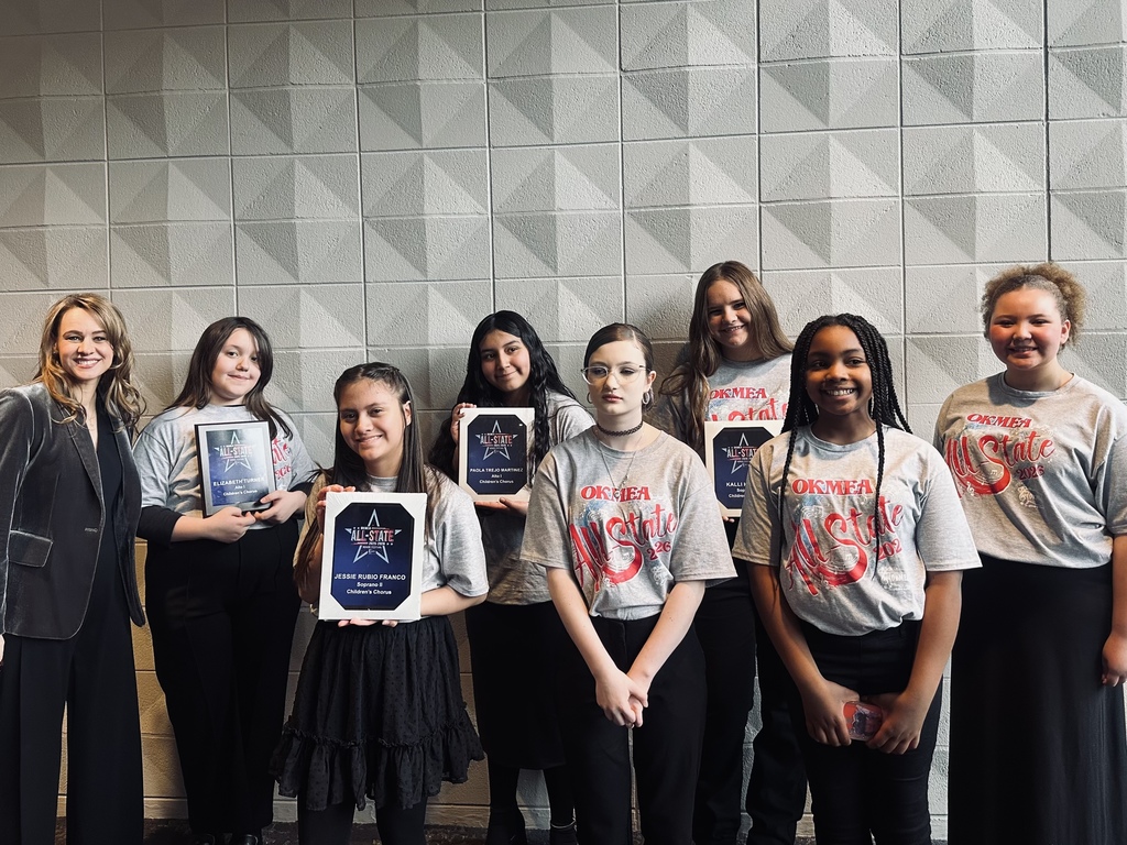 Group of young women and a woman holding awards in front of a wall.