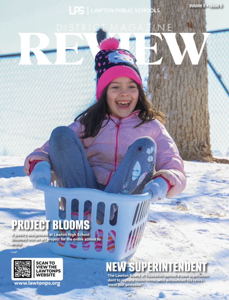 Girl in pink jacket and hat sits in a laundry basket on snow. Magazine cover reads "Review" and "Project Blooms."