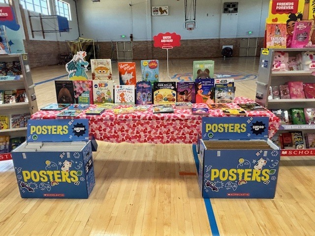 A table with books on a red tablecloth in a room with shelves of books and boxes labeled "Posters".