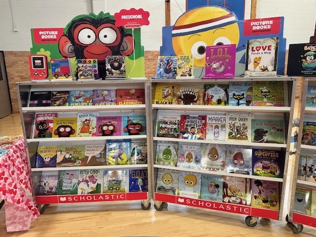 Two movable bookshelves with colorful books and toys. A sign at the top reads "Scholastic".