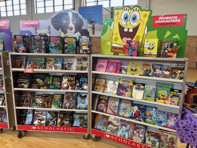 Two shelves filled with children's books, toys, and DVDs. One shelf features a dog. A colorful cartoon character sign above the books.