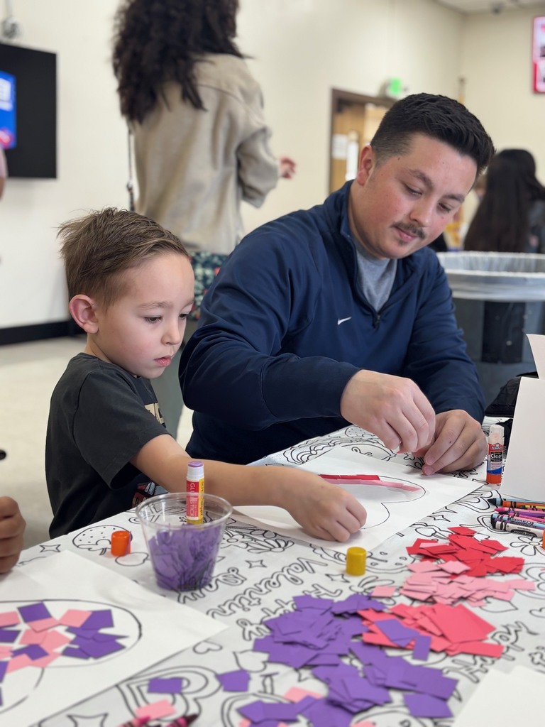 Adult and child seated at a table, creating a paper collage with colored paper and glue.