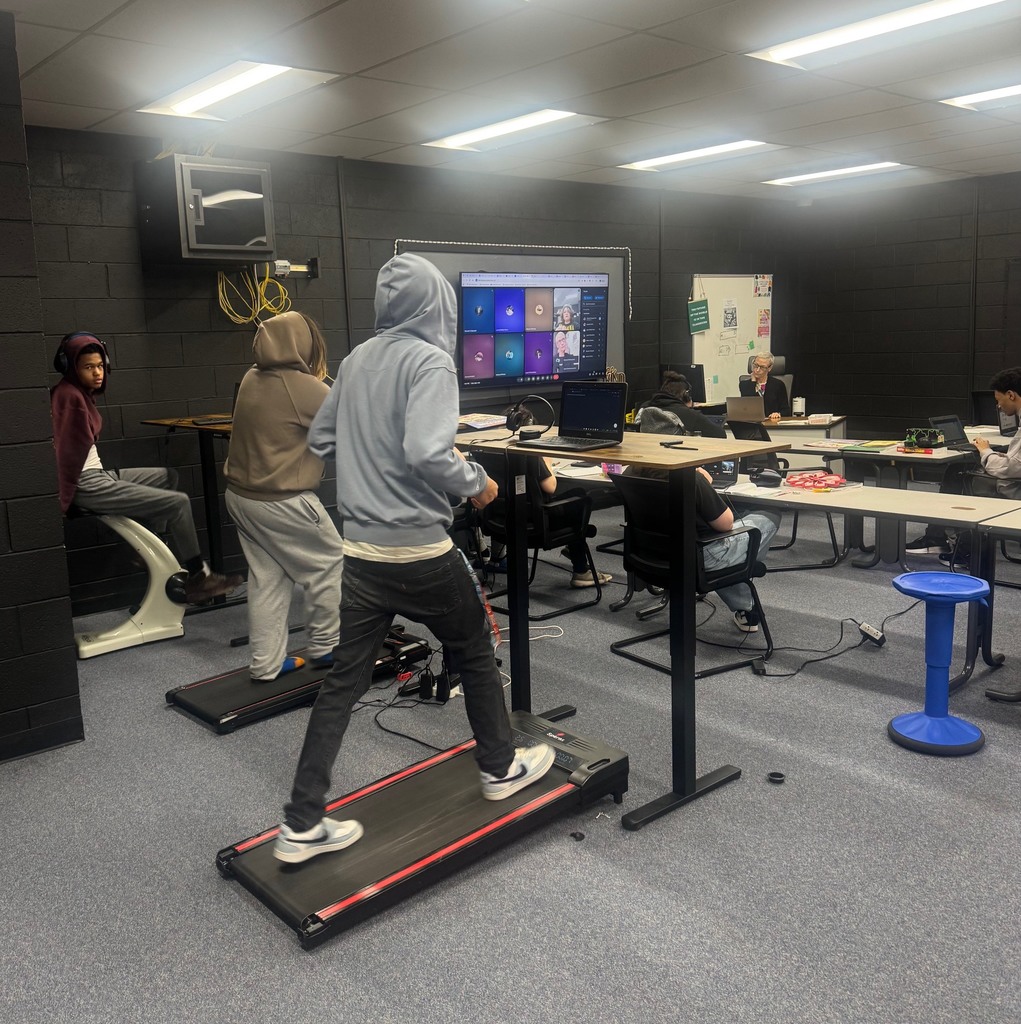 A person in a gray hoodie and black pants runs on a treadmill in a room.