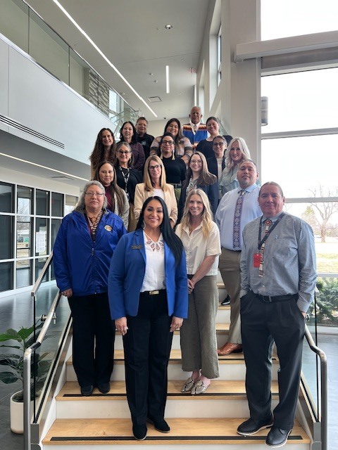 A group of people dressed in business attire stand on stairs in a modern office building.