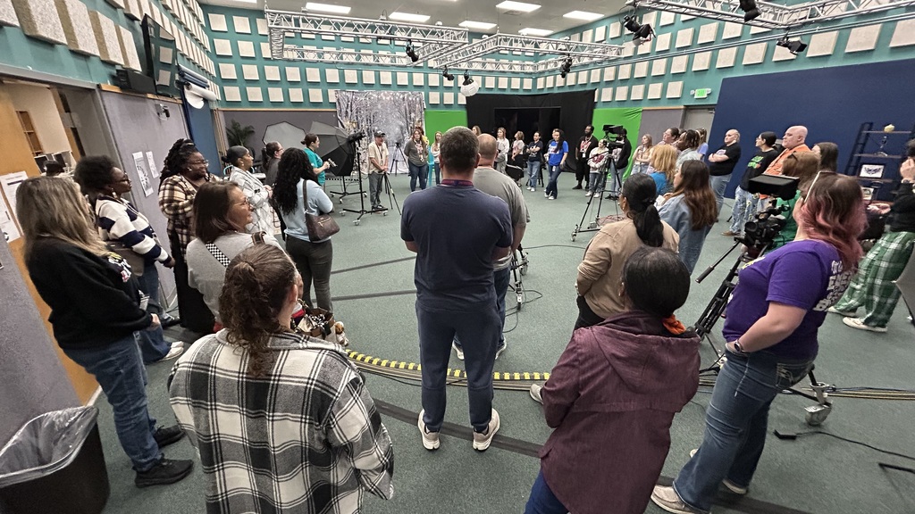 Group of people gathered in a circle inside a studio with green screen backdrop.