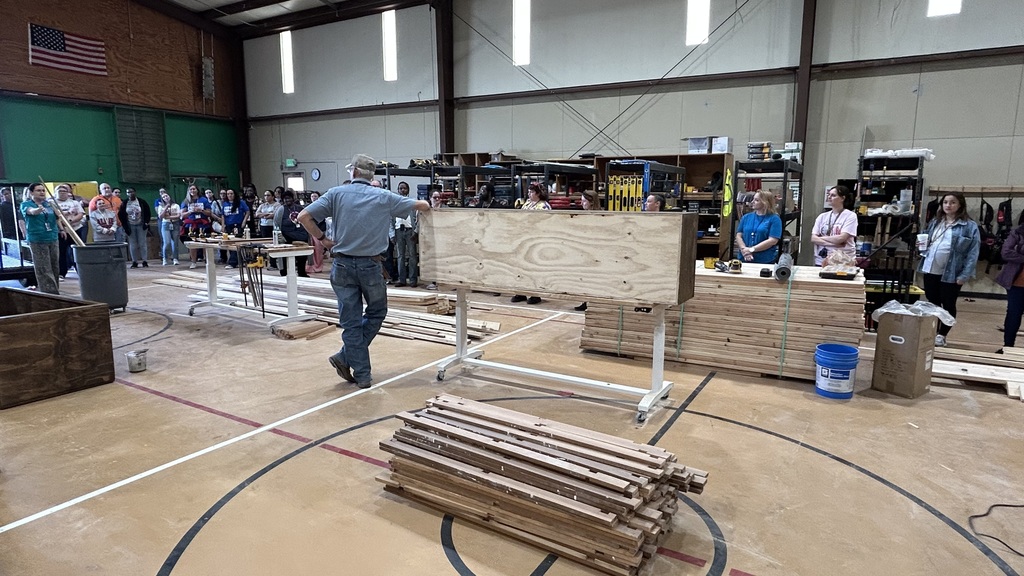 A group of people in a gym, one person working on a wooden board, others observing.