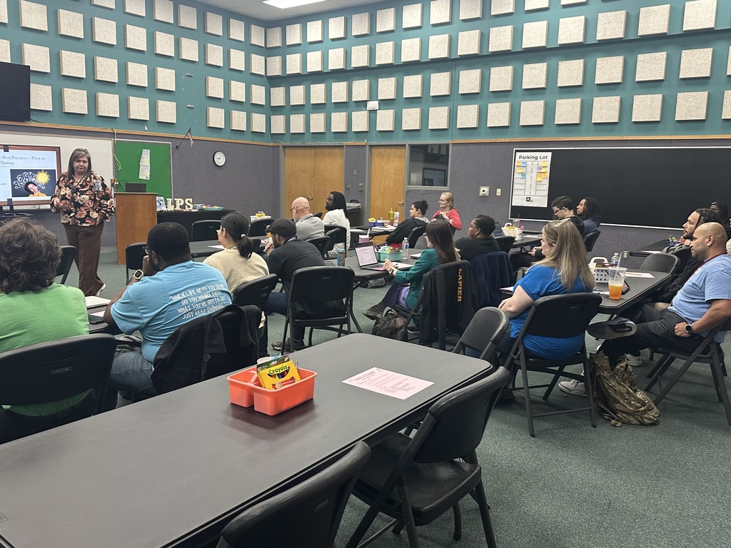 Group of people in a classroom with a woman standing at a podium in front of a screen.