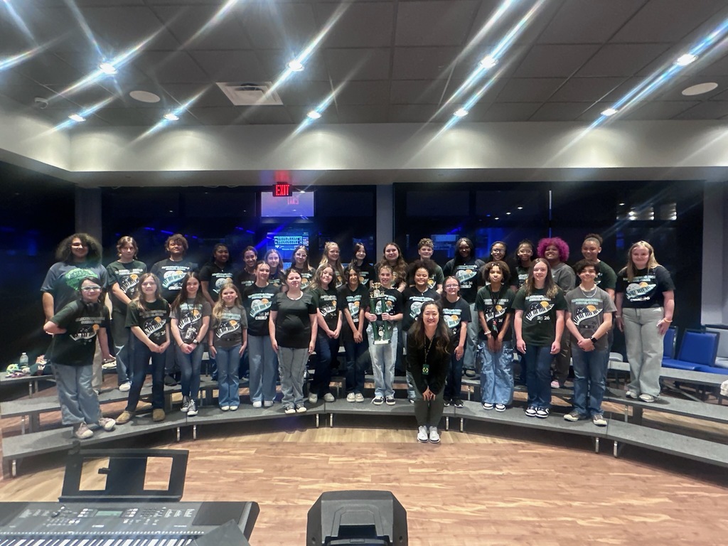 Large group of people wearing matching shirts standing in a semicircle on a stage with musical instruments.