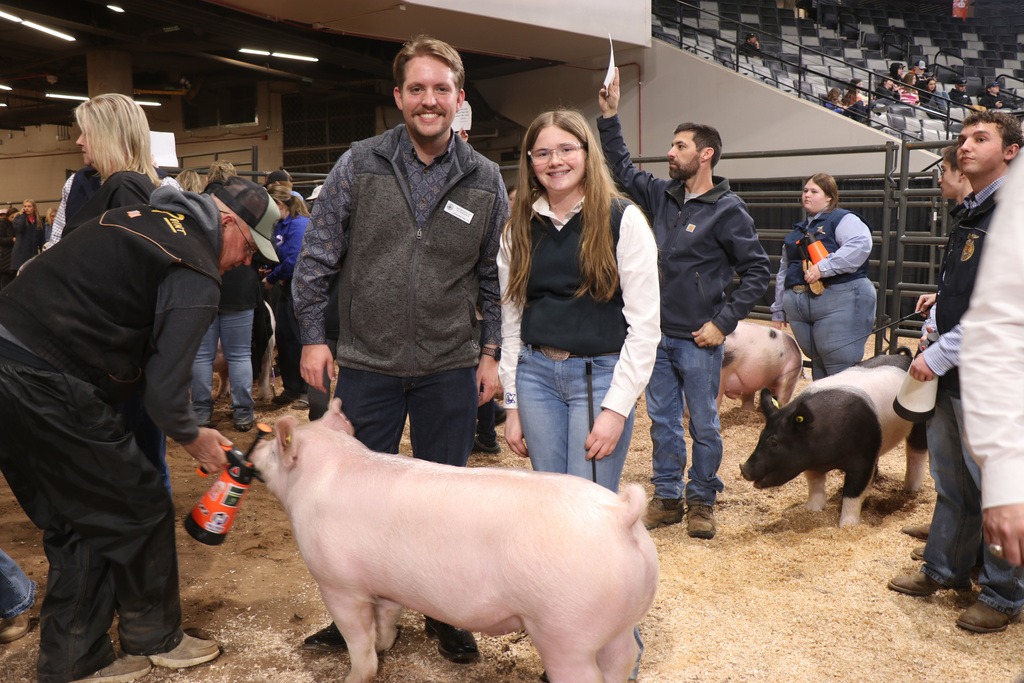 People stand around a pig at an event. One person looks at it while another holds a sign.