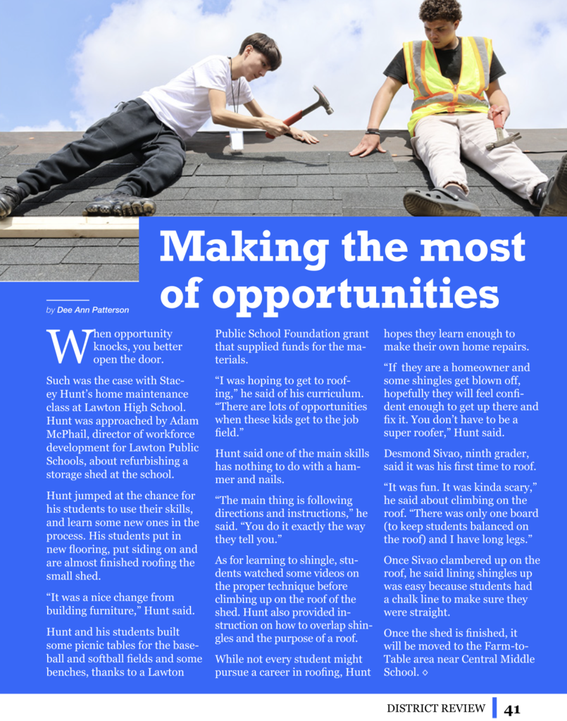 Two males students on a roof. One holding a hammer and the other in a safety vest holding the shingle.