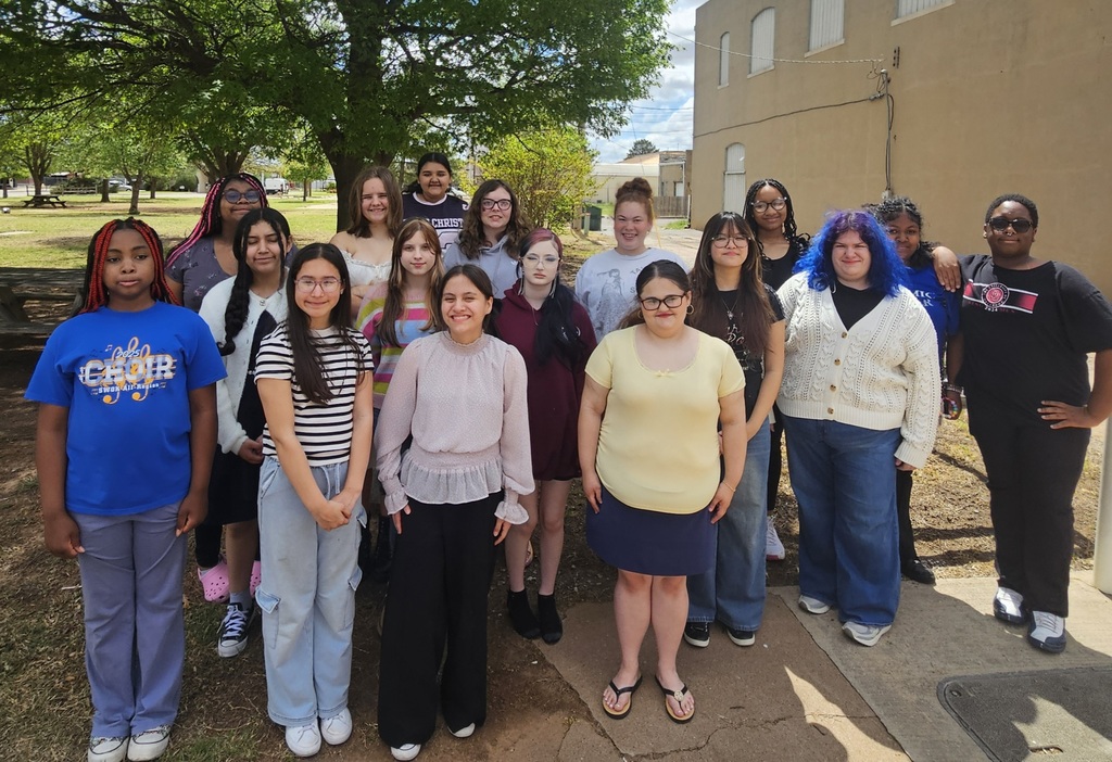 A group of people stands in front of a building, some wearing glasses and sneakers.