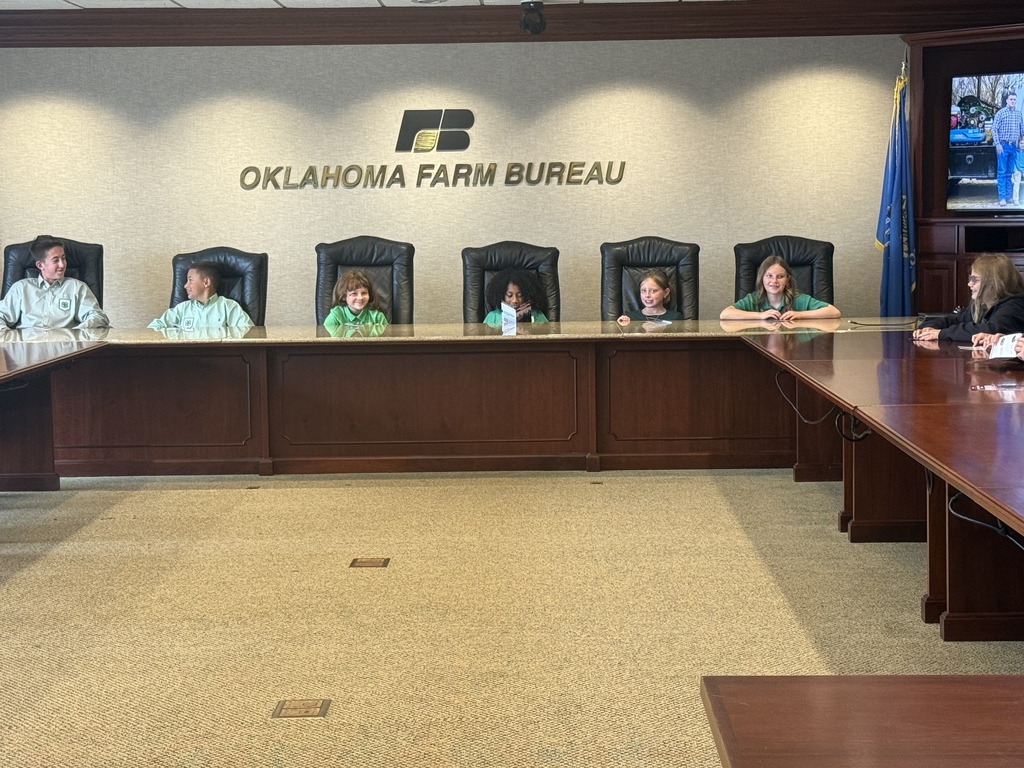 A conference room with six people seated at a long table. An "OKLAHOMA FARM BUREAU" sign is at the top of the wall.