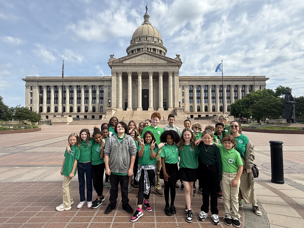 A group of children in green T-shirts and pants standing outside a building with a dome roof.