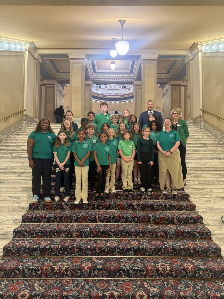 A group of children in green shirts and pants pose on a staircase in a building.
