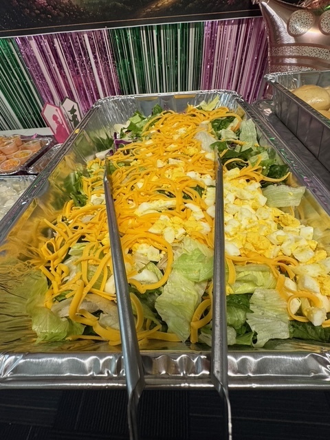 Tray of salad with shredded carrots and eggs, arranged on a black surface. Colorful decorations in background.