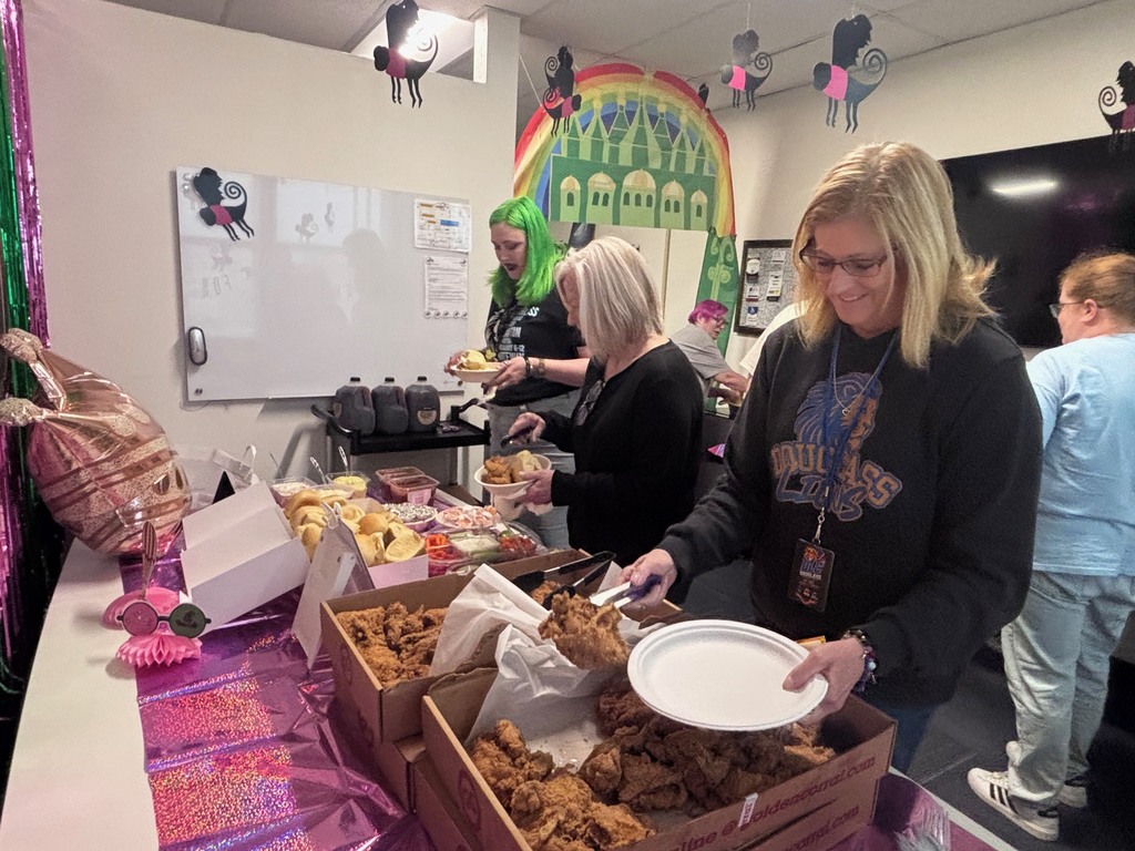 A woman stands at a table holding a plate with food, while others gather around food displays.