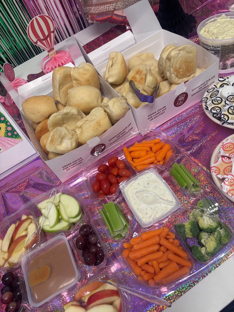 A table with two boxes of sandwiches, assorted vegetables, dips, and fruits in plastic containers.