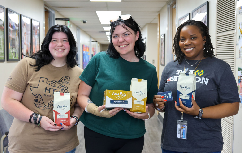 Three women in a hallway, each holding a box, standing next to each other.