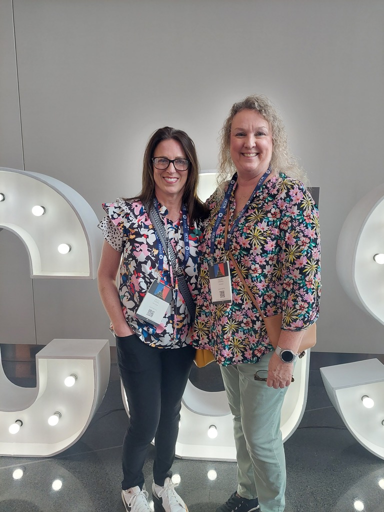 Two women in front of a large light display spelling out "CS". 