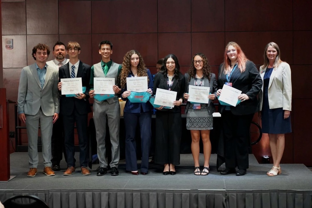 A group of people holding certificates on stage, possibly for an award ceremony. They are wearing formal attire.