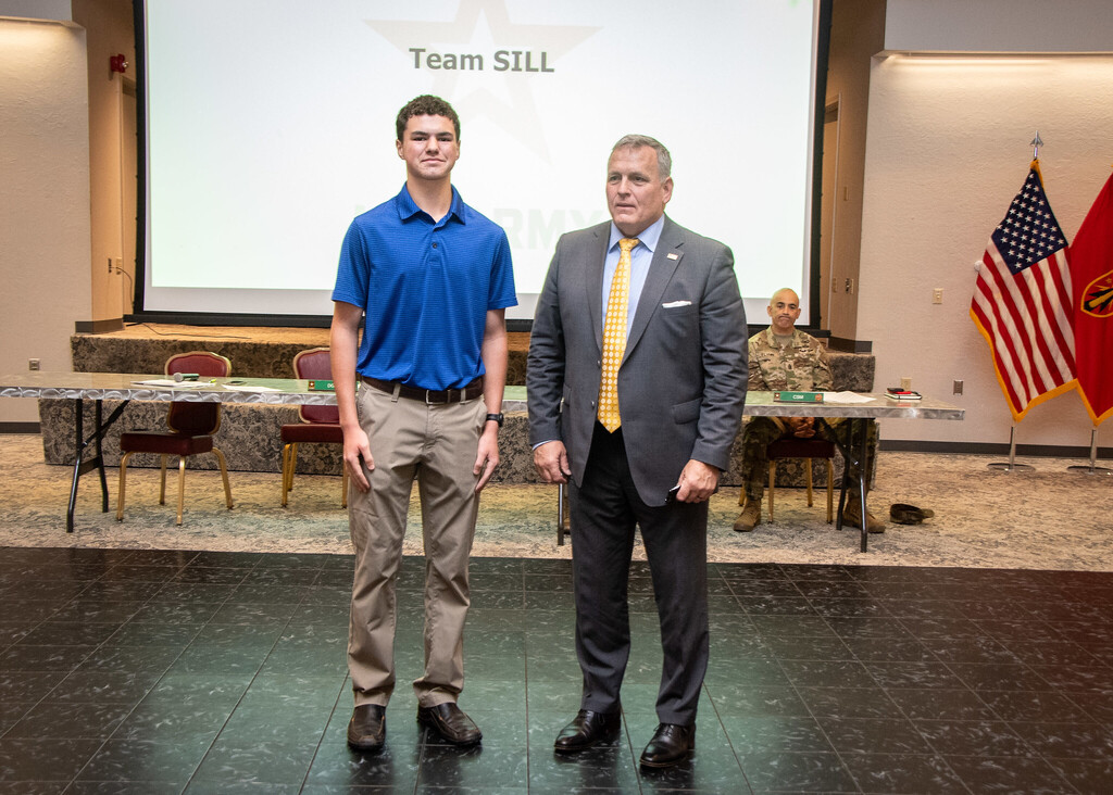 Two men, one in a blue shirt and the other in a gray suit, stand on a stage.