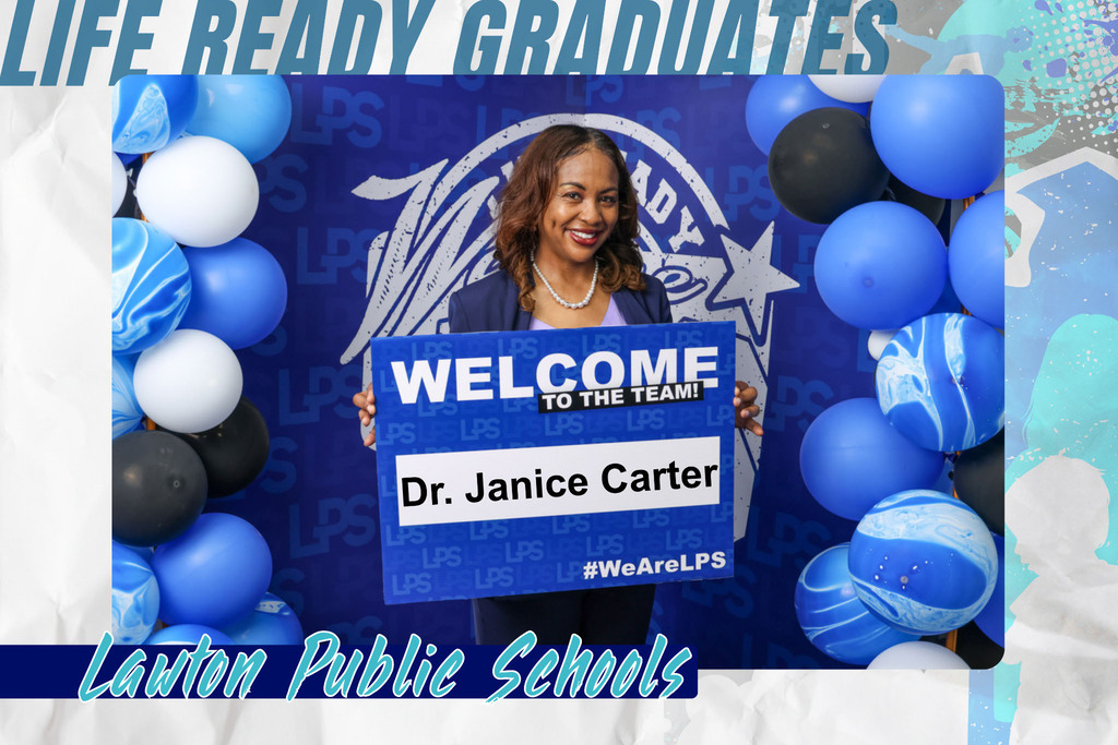 A woman holds a blue sign reading "WELCOME TO THE TEAM" with "Dr. Janice Carter" underneath. Behind her, a backdrop with a school logo and balloons.