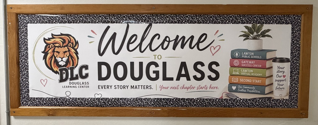A wooden framed sign reads "Welcome to DLC Douglass". It features a lion and books. A plant is next to the books.