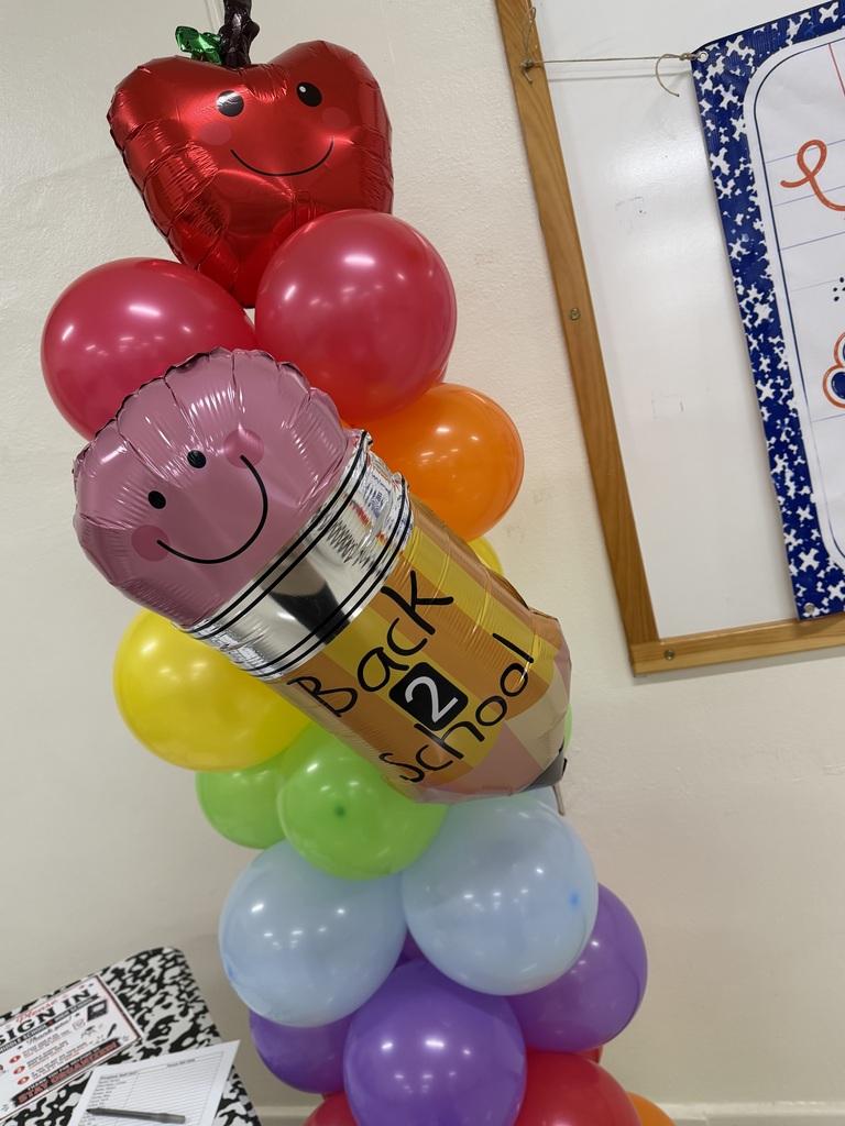 A balloon bouquet with a pencil balloon at the top, surrounded by colorful balloons, including red, yellow, and purple.