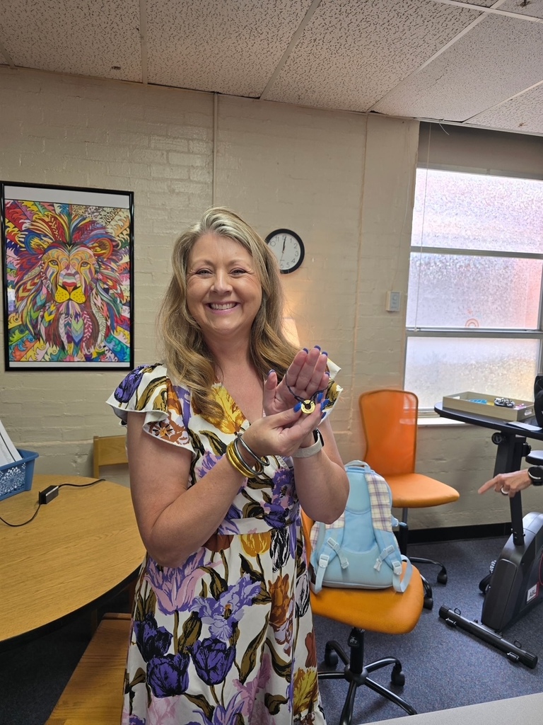 Woman in a floral dress holds a bracelet in a room with an orange chair.