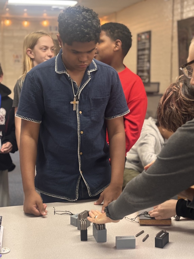 A classroom with students working together around a table with small pieces. One student is holding a piece.