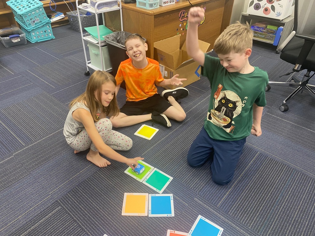 Three children, two girls and one boy, play with colorful blocks on a carpeted floor.