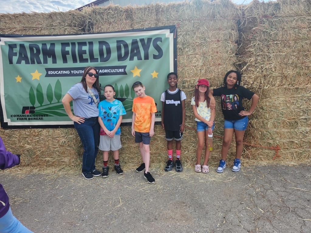 Six people stand next to a large haystack. A banner reading "Farm Field Days" is behind them.