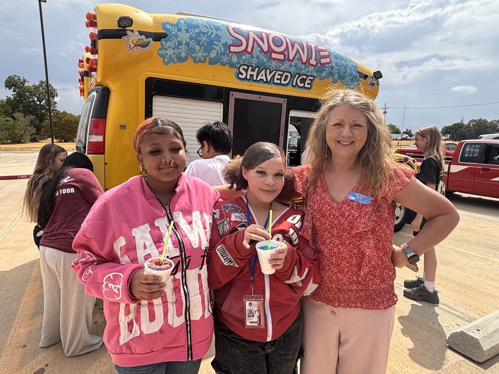 Three people stand together in front of a shaved ice truck. Two girls hold cups of shaved ice.