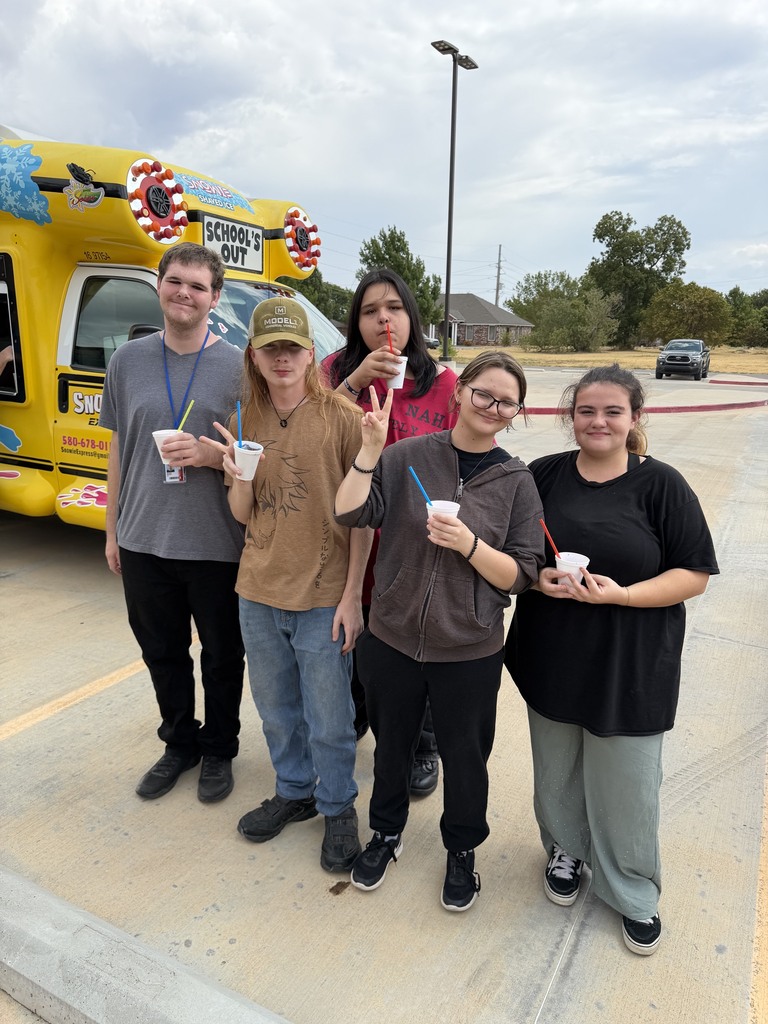Five individuals stand in a parking lot, holding cups. A yellow ice cream truck is in the background.