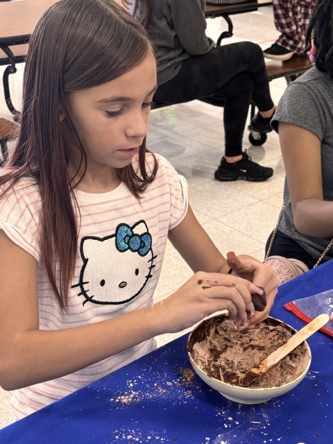 Girl in a Hello Kitty shirt mixes chocolate in a bowl with a wooden spoon.
