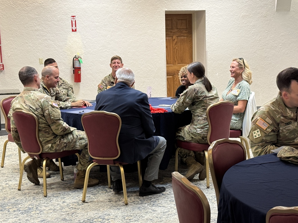 A group of individuals in military uniforms and business attire gathered around a table in a room.