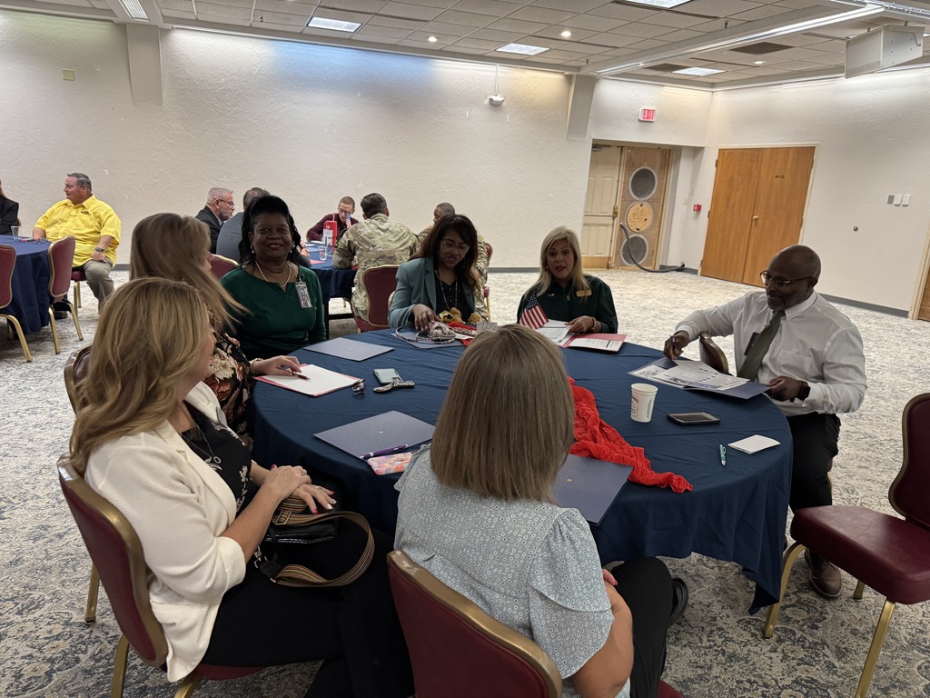Group of people sitting around a round table in a conference room. Some are looking at papers.
