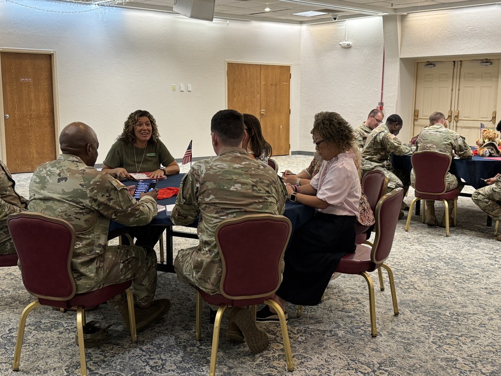 A group of people in military uniforms and civilian clothes sit at a table in a room.