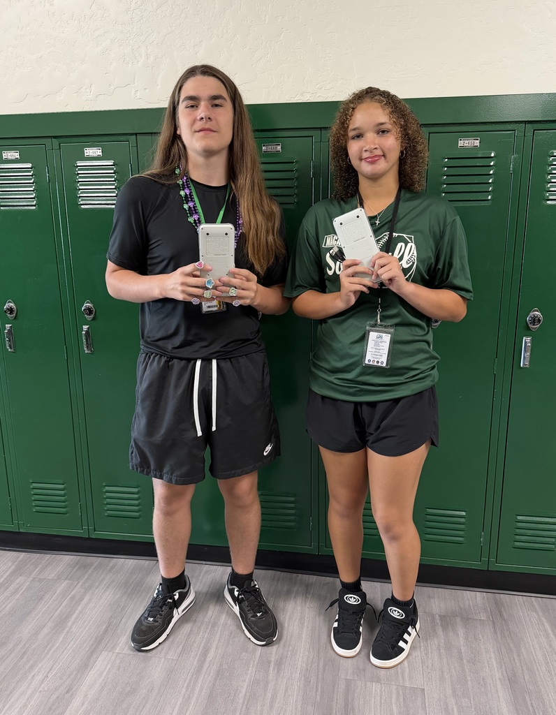 Two people stand by lockers; one holds a phone, and the other shows a card. They both wear sneakers.