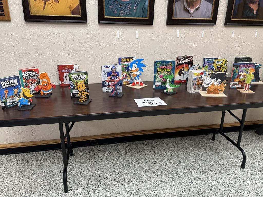 A table with many figurines, including Sonic, displayed in a room with framed pictures on the wall.