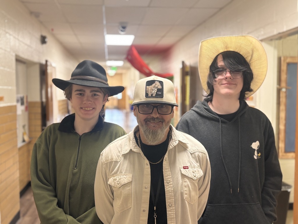 Three people in hats stand in a hallway with walls, a door, and a bright light.