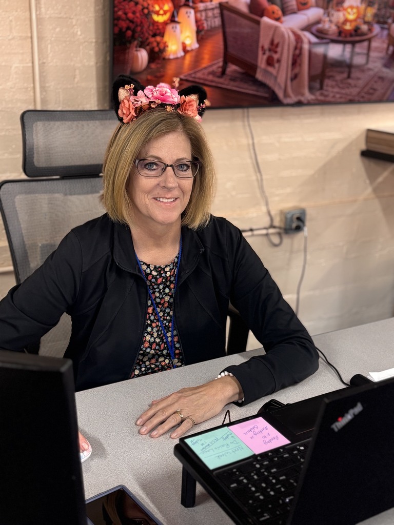 Woman wearing Minnie Mouse ears sits at desk, smiling, with computer and papers in front.