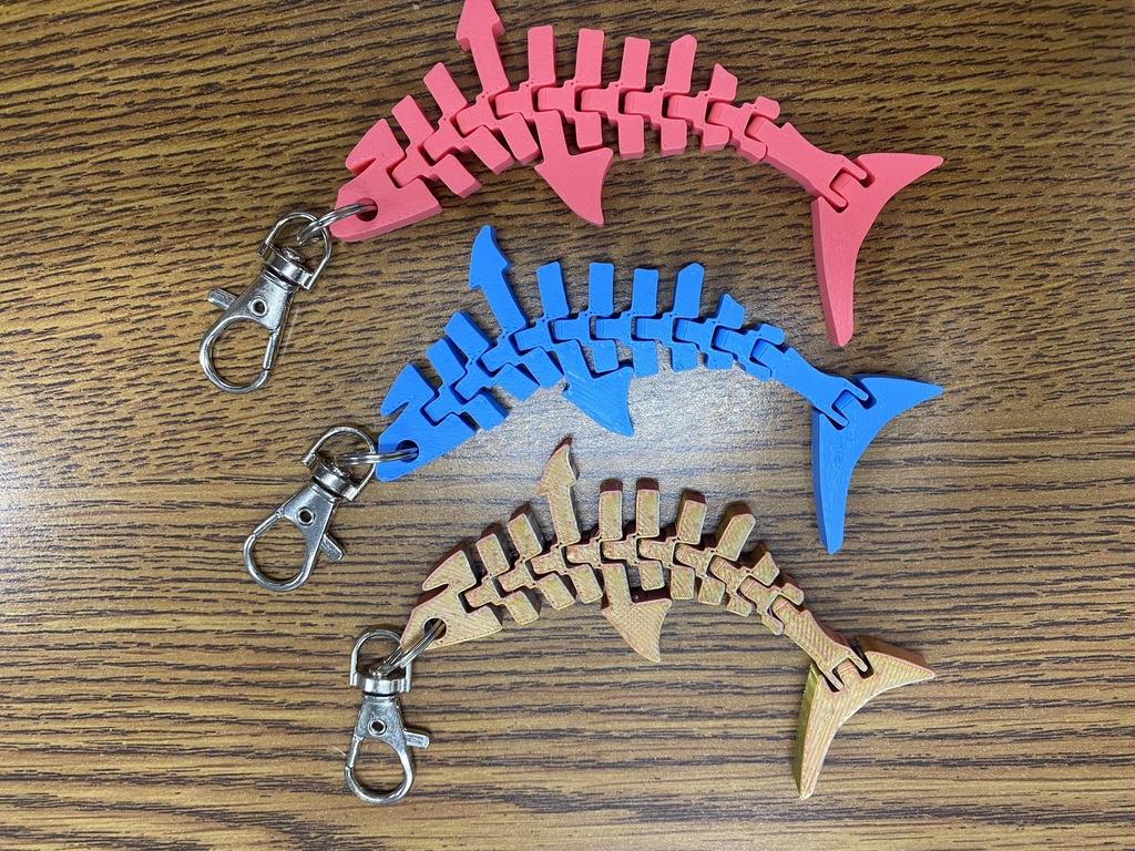 Four wooden shark-shaped keychains, in different colors, on a brown wood surface.