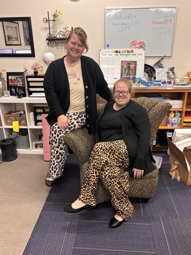 Two women in leopard-print pants sitting in a chair; one wears a cardigan, the other a black sweater.