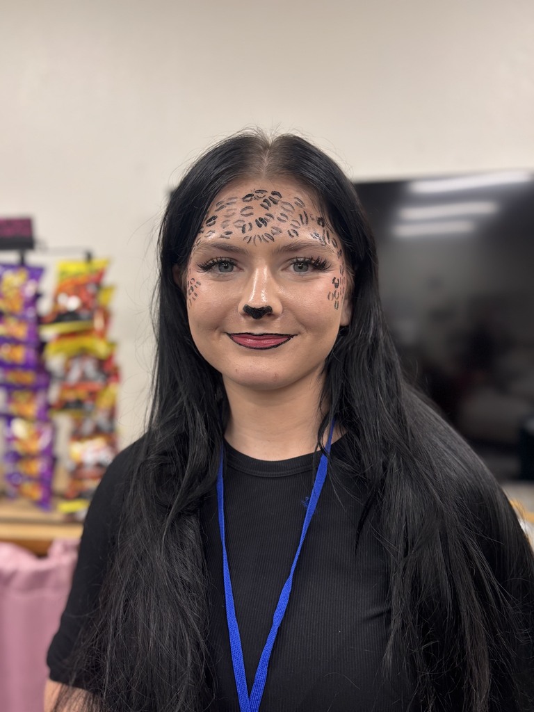 Woman with face paint and black t-shirt with blue lanyard standing in front of shelves.