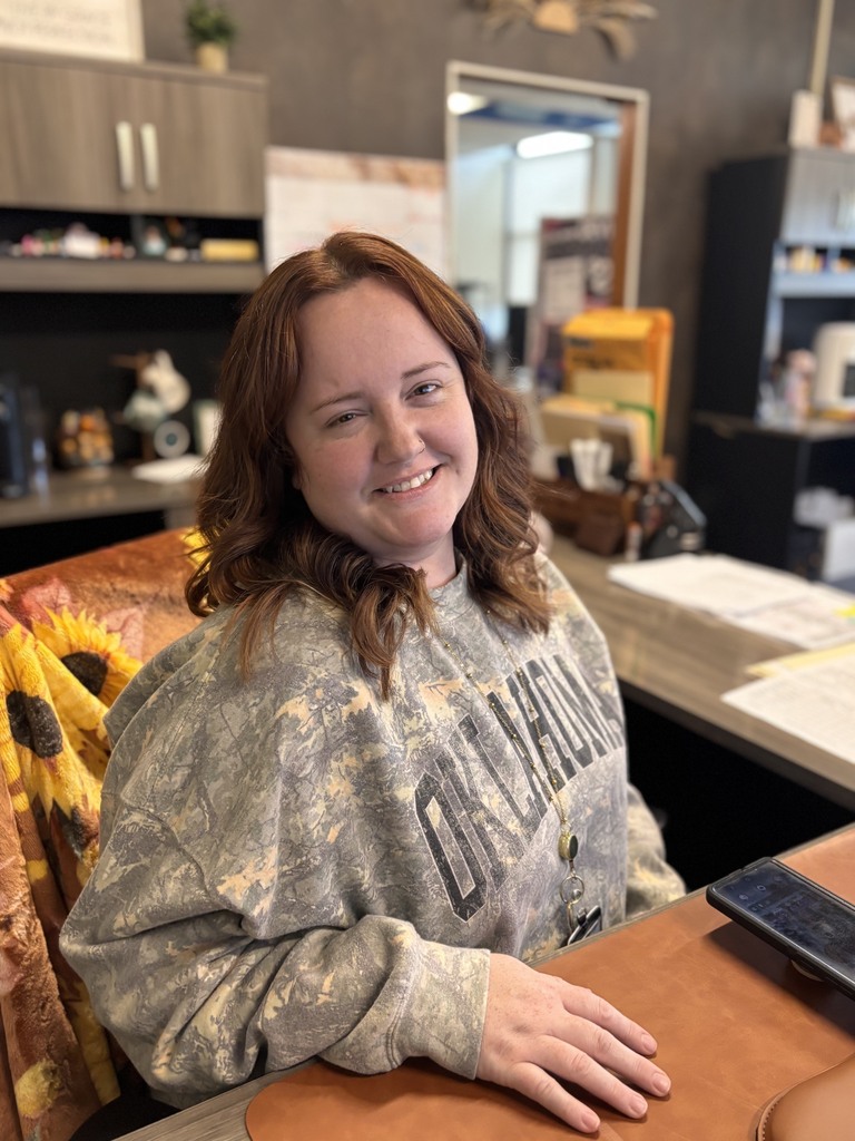 Woman with brown hair sits at a desk with a smile, a phone in front, and a sunflower blanket behind.