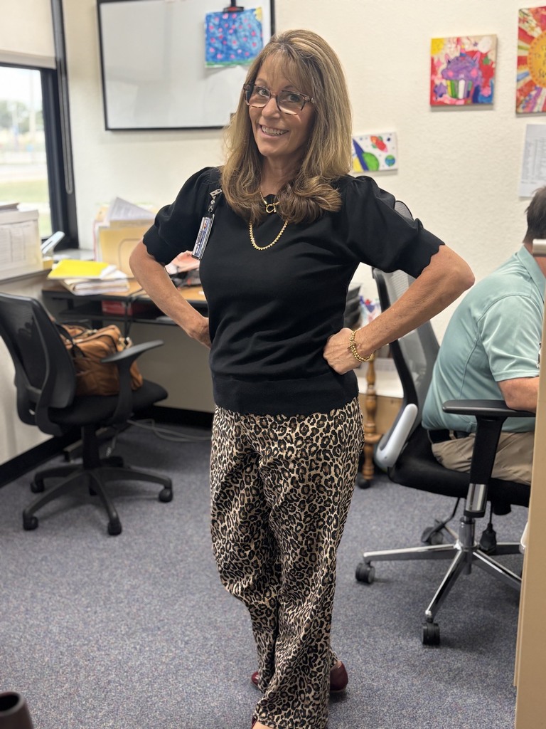 Woman in glasses and leopard-print pants stands with hands on hips in an office.