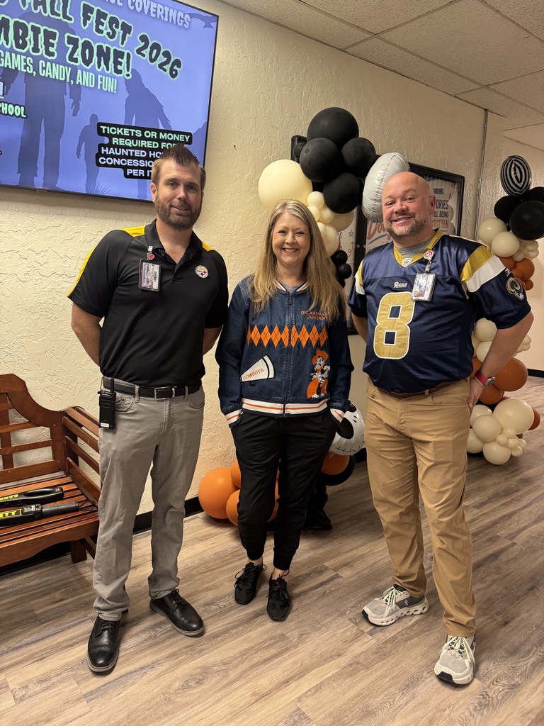 Three adults standing next to each other, smiling. Behind them are decorations including balloons and pumpkins.